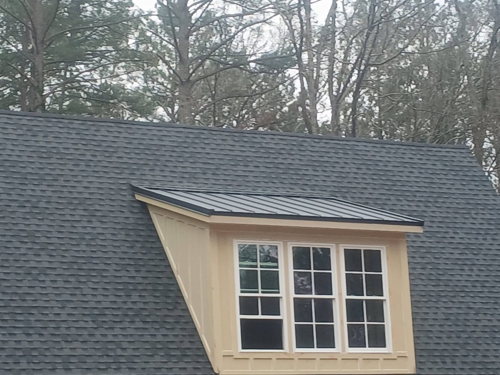 Close detail of a shingle roof meeting a standing seam metal dormer roof
