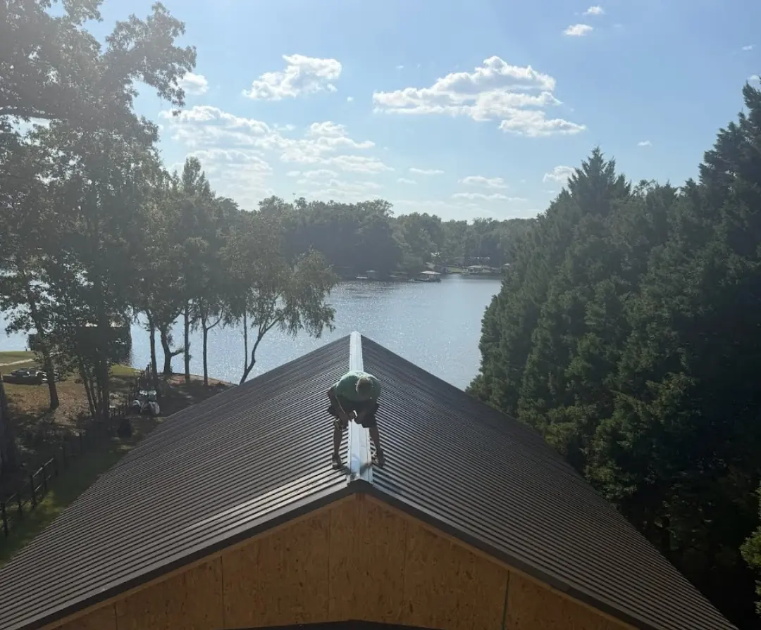 Crew member installing the ridge cap on a brown metal roof with a lake in the background