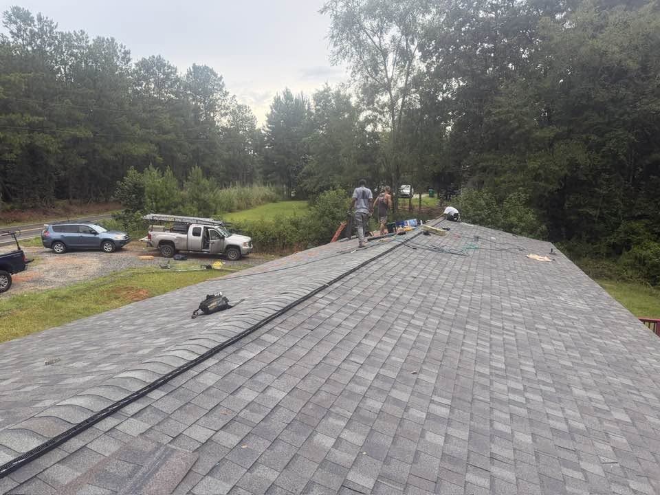 Shingle roof installation in progress with ridge vent being set