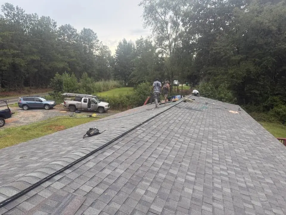 Shingle roof installation in progress with ridge vent being set